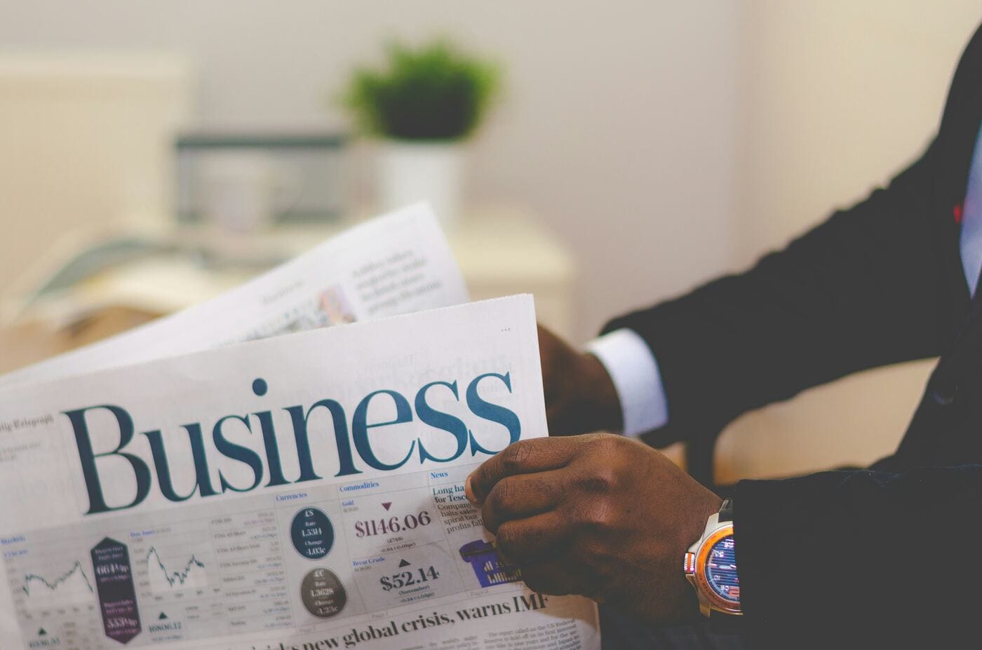 A hand holding a folded newspaper with a Business section and market data, representing the reporting sent to the bureaus each cycle