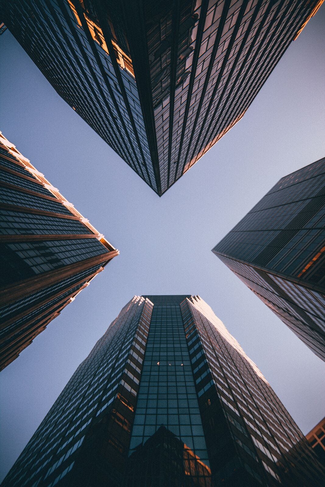 Looking straight up at four modern glass skyscrapers converging toward the sky, representing corporate formation and growth