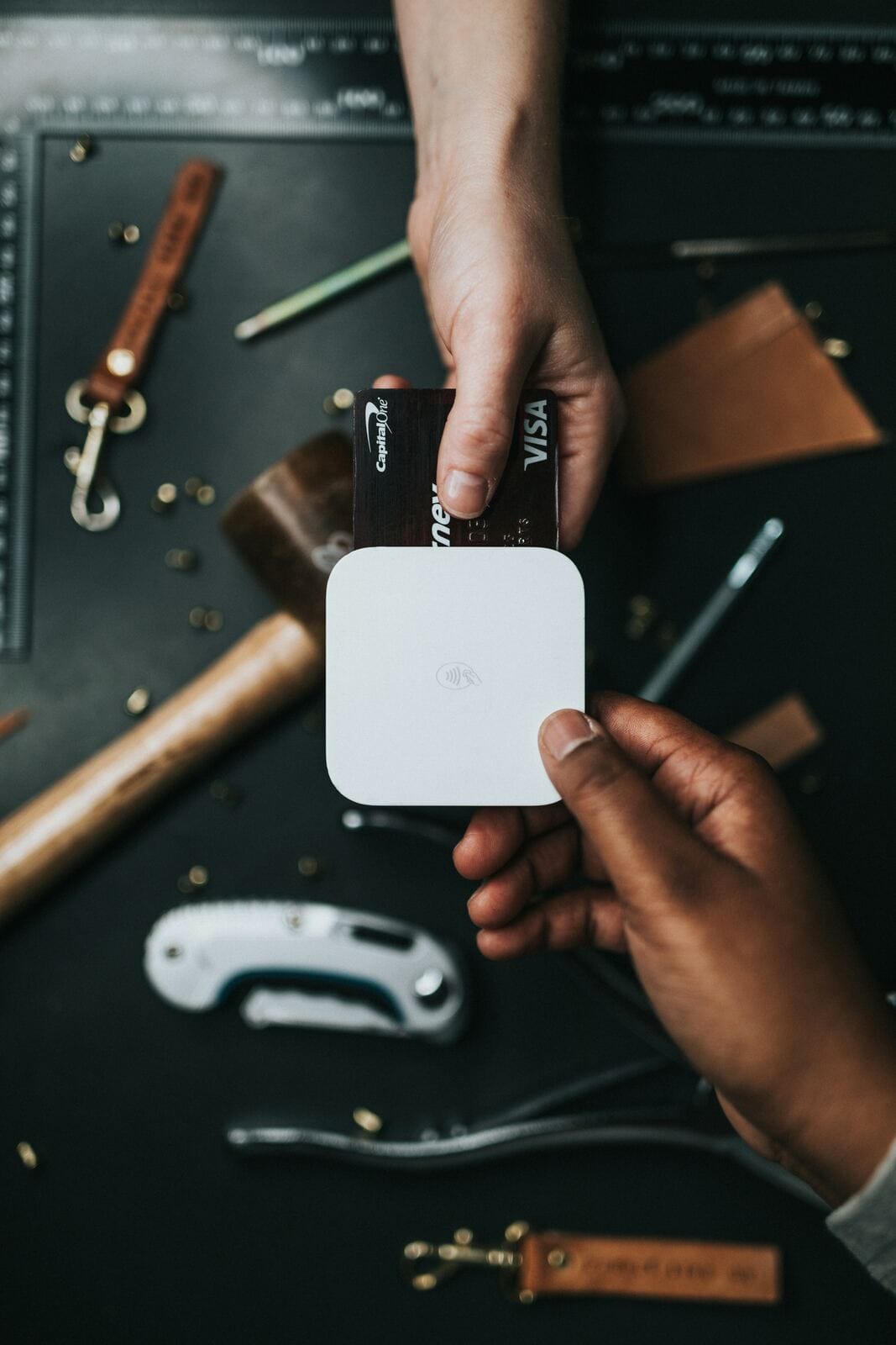A small business owner tapping a credit card against a wireless payment reader at a workbench