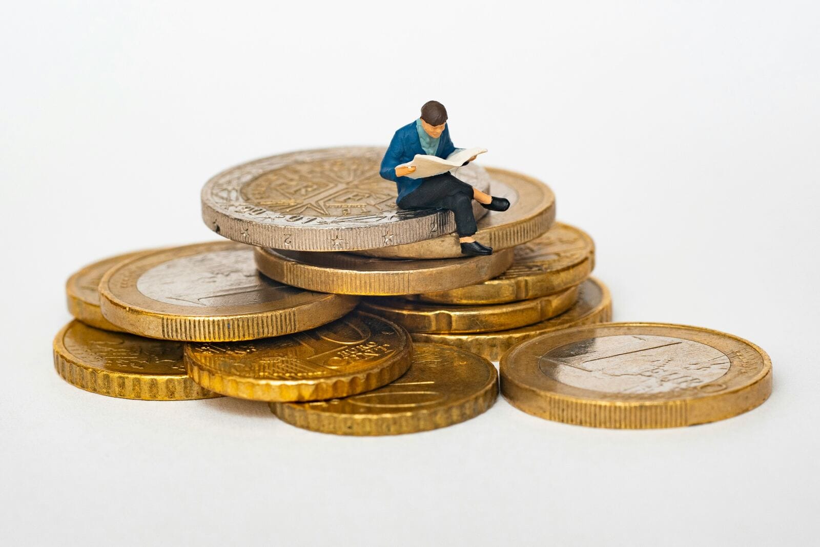 A small figurine sitting atop a stack of coins, reading a newspaper, representing financial press coverage